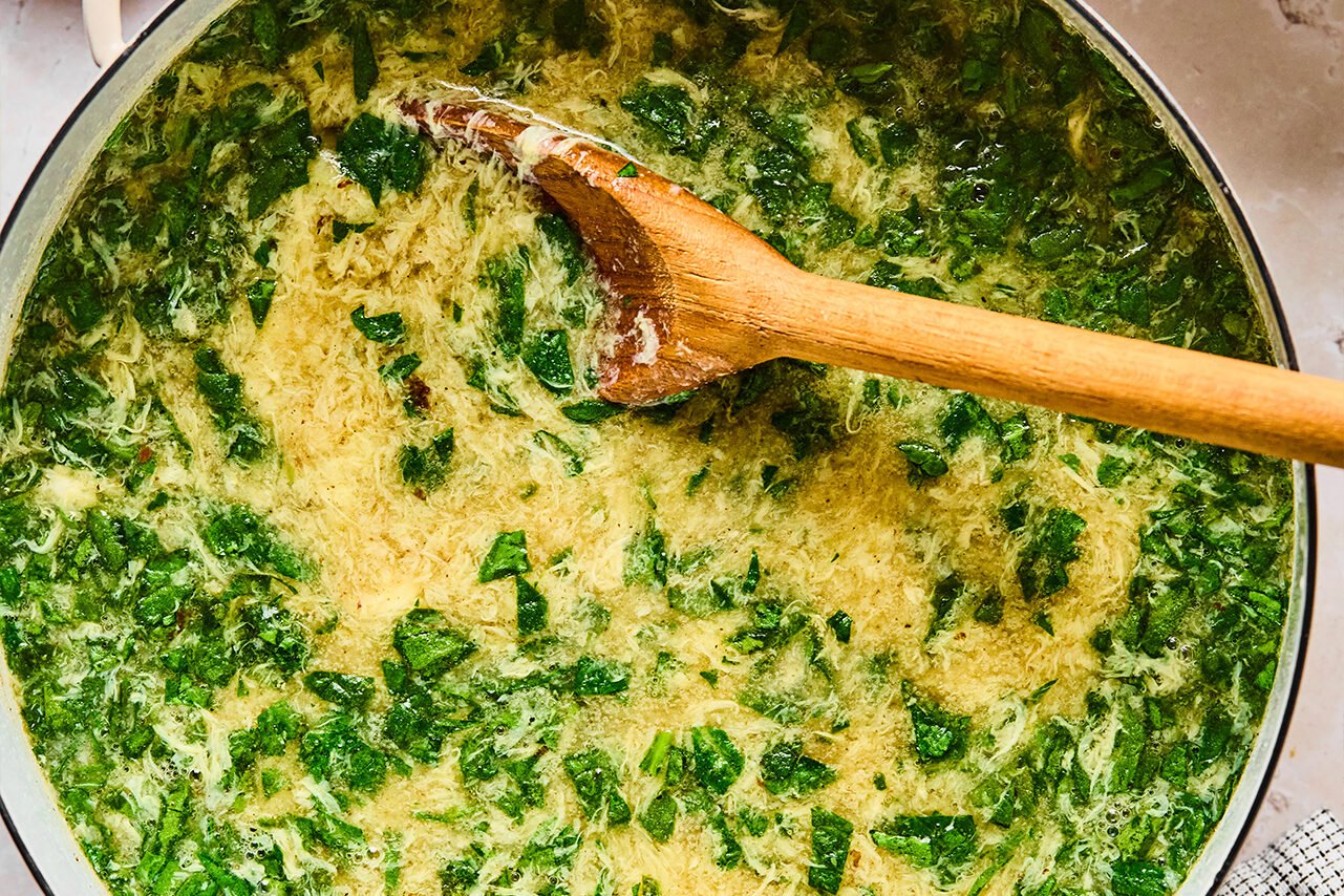 The soup with spinach wilted in it and a wooden spoon stirring it.