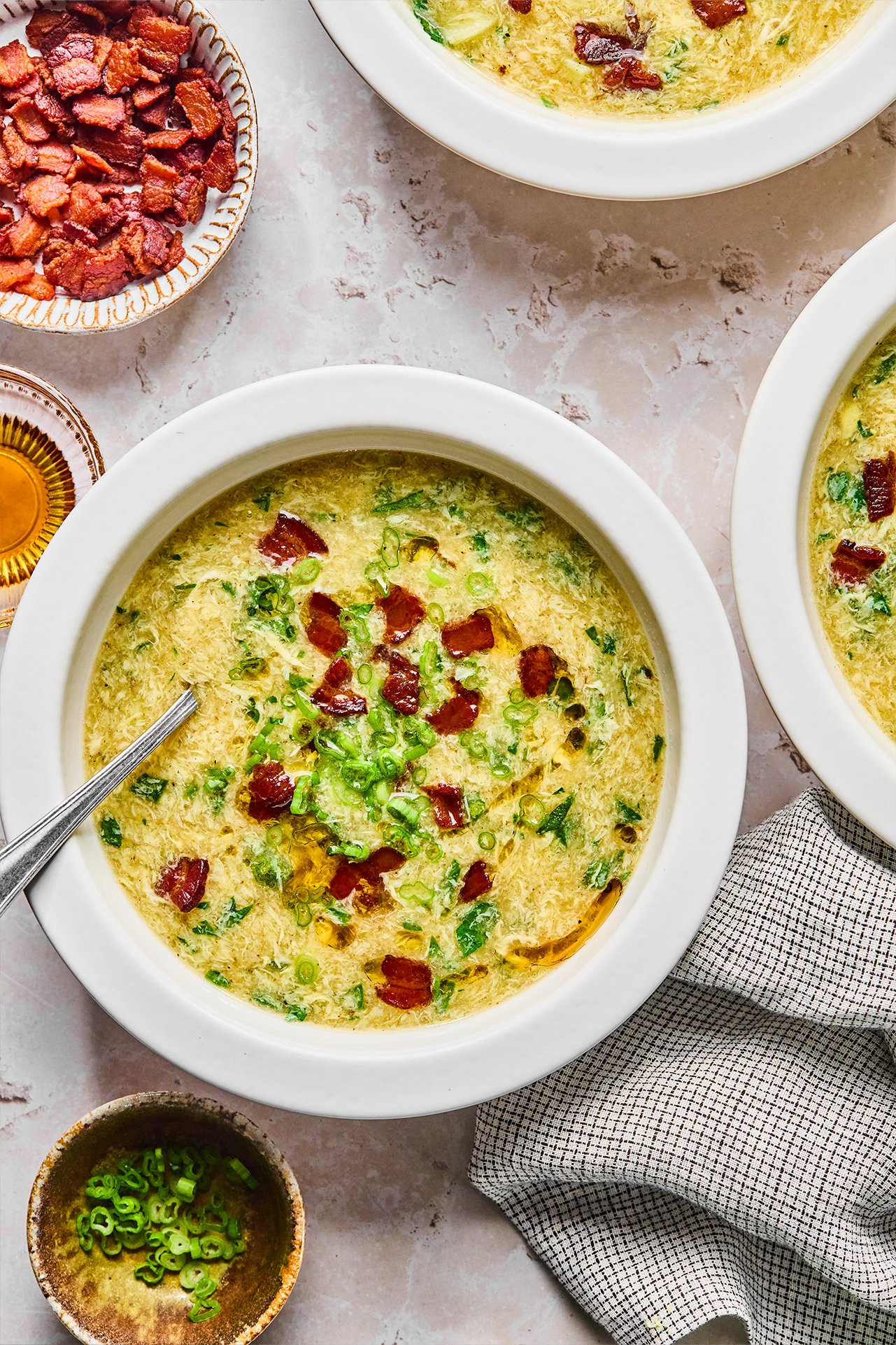 Breakfast egg drop soup in a bowl topped with bacon and green onion, with bacon on the side.