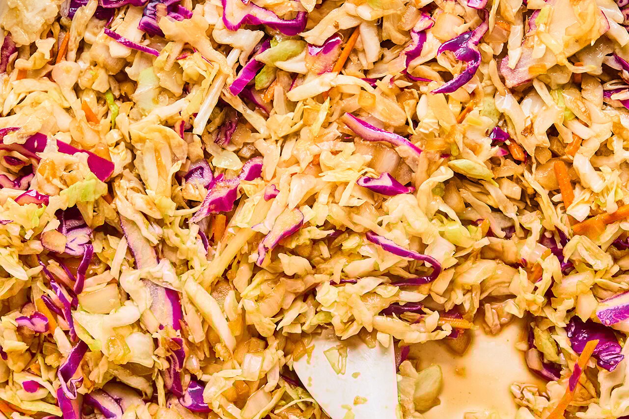 The coleslaw mix and coconut aminos added into the pan to saute with the onions, garlic, and ginger.