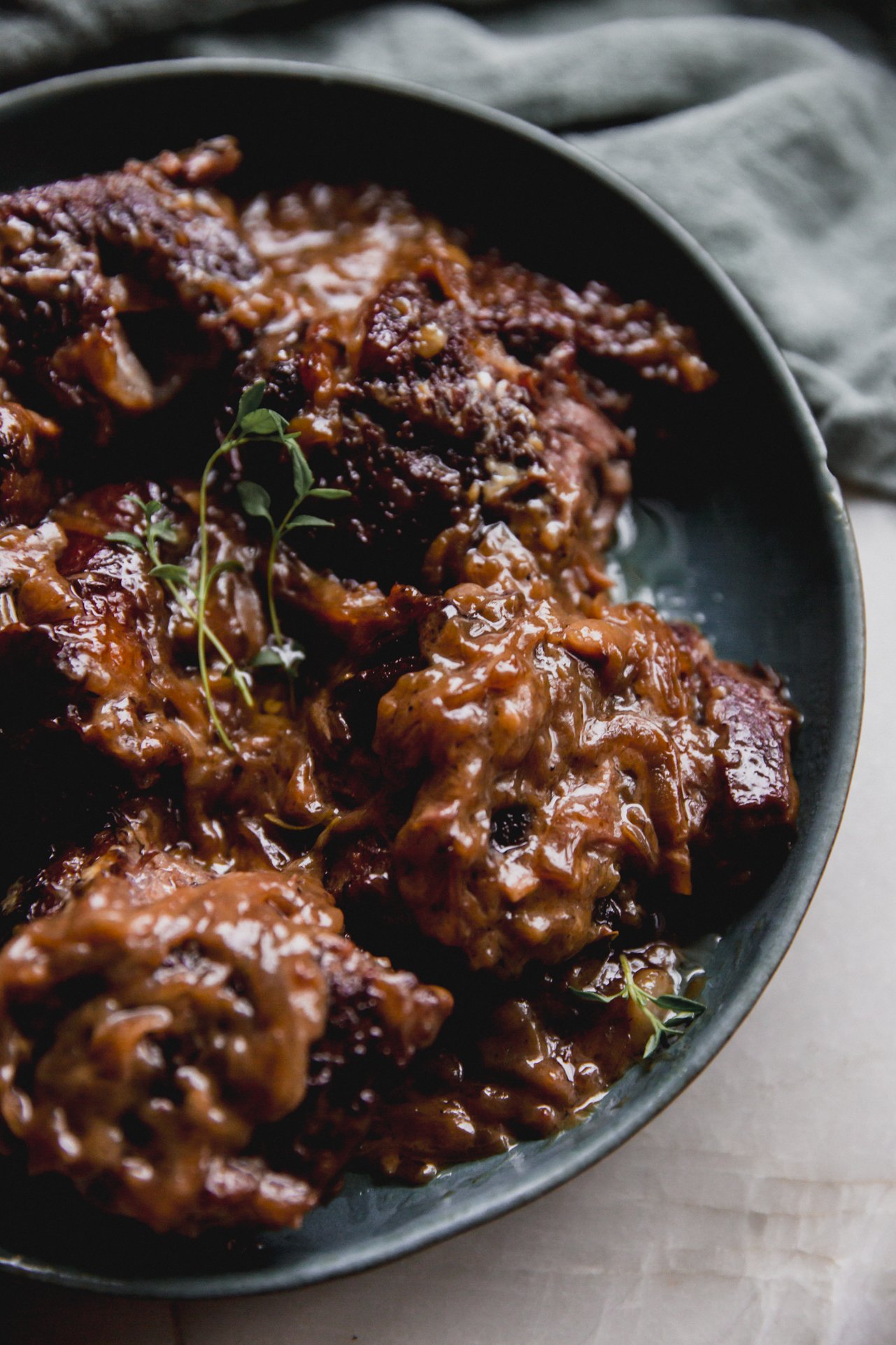 French onion short ribs in a green bowl, shredded and topped with fresh thyme.