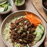 Korean beef bowl with ground beef, carrots, cucumber and caulfilower rice with more toppings in bowls on the side.