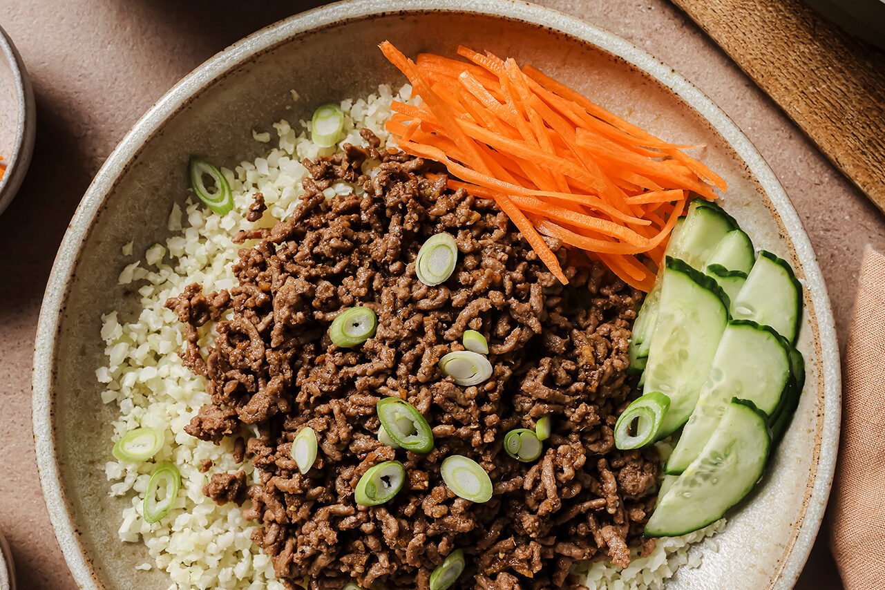 Korean beef bowls in a bowl with cucumber, carrots, and cauliflower rice.