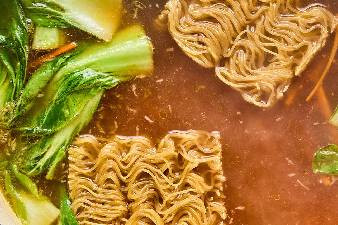 Ramen and broth added into the bok choy and carrots in the pan.