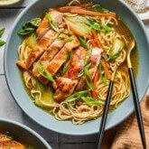 Teriyaki chicken ramen in a bowl with sliced chicken on top, green onions and ramen and veggies in the bowl.