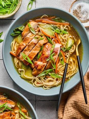 Teriyaki chicken ramen in a bowl with sliced chicken on top, green onions and ramen and veggies in the bowl.
