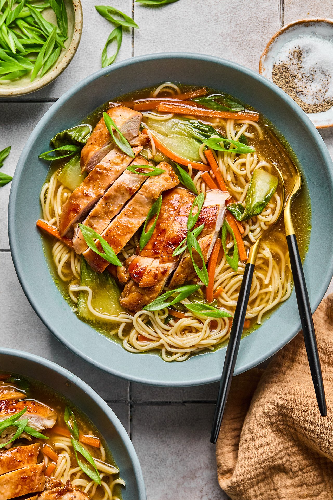 Teriyaki chicken ramen in a bowl with sliced chicken on top, green onions and ramen and veggies in the bowl.