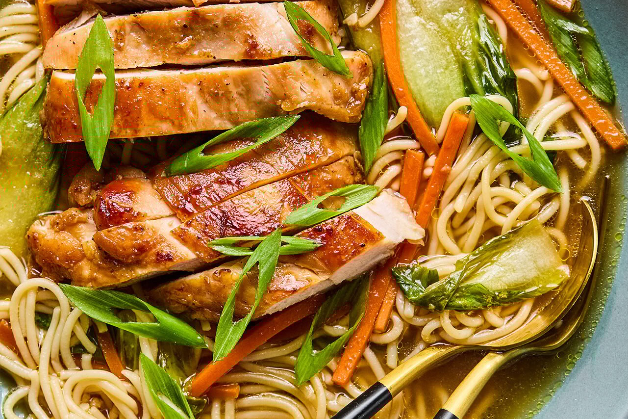 The final dish with broth, ramen, vegetables, and chicken in it and a spoon ready to dig in.