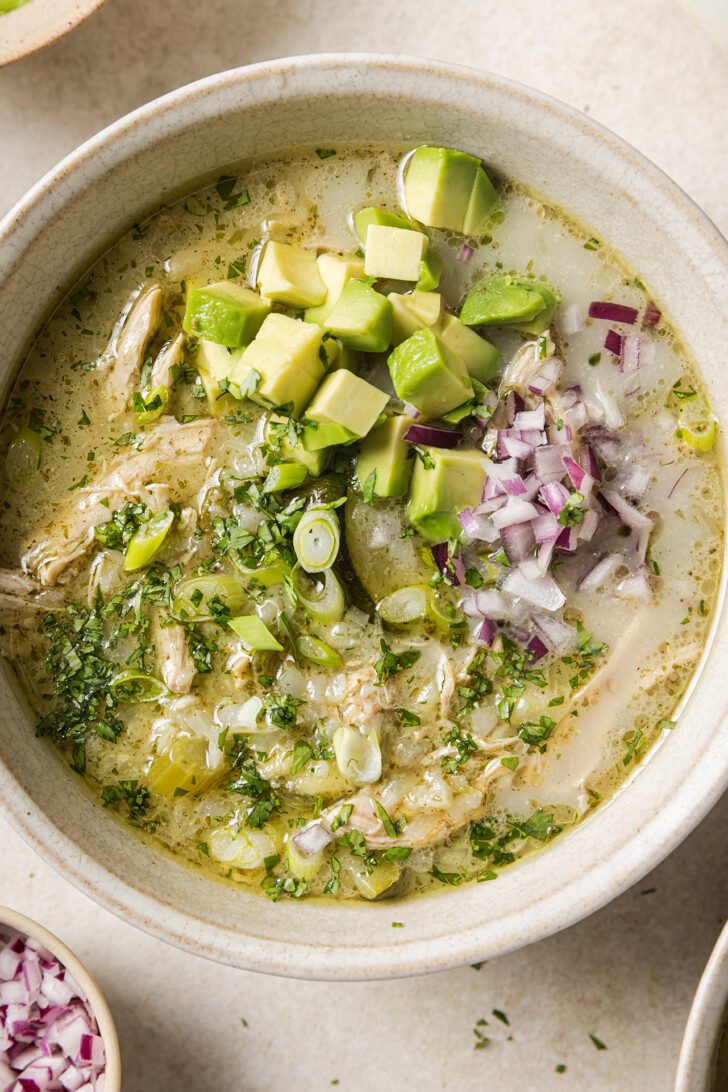 A bowl of white chicken chili topped with red onion and avocado.