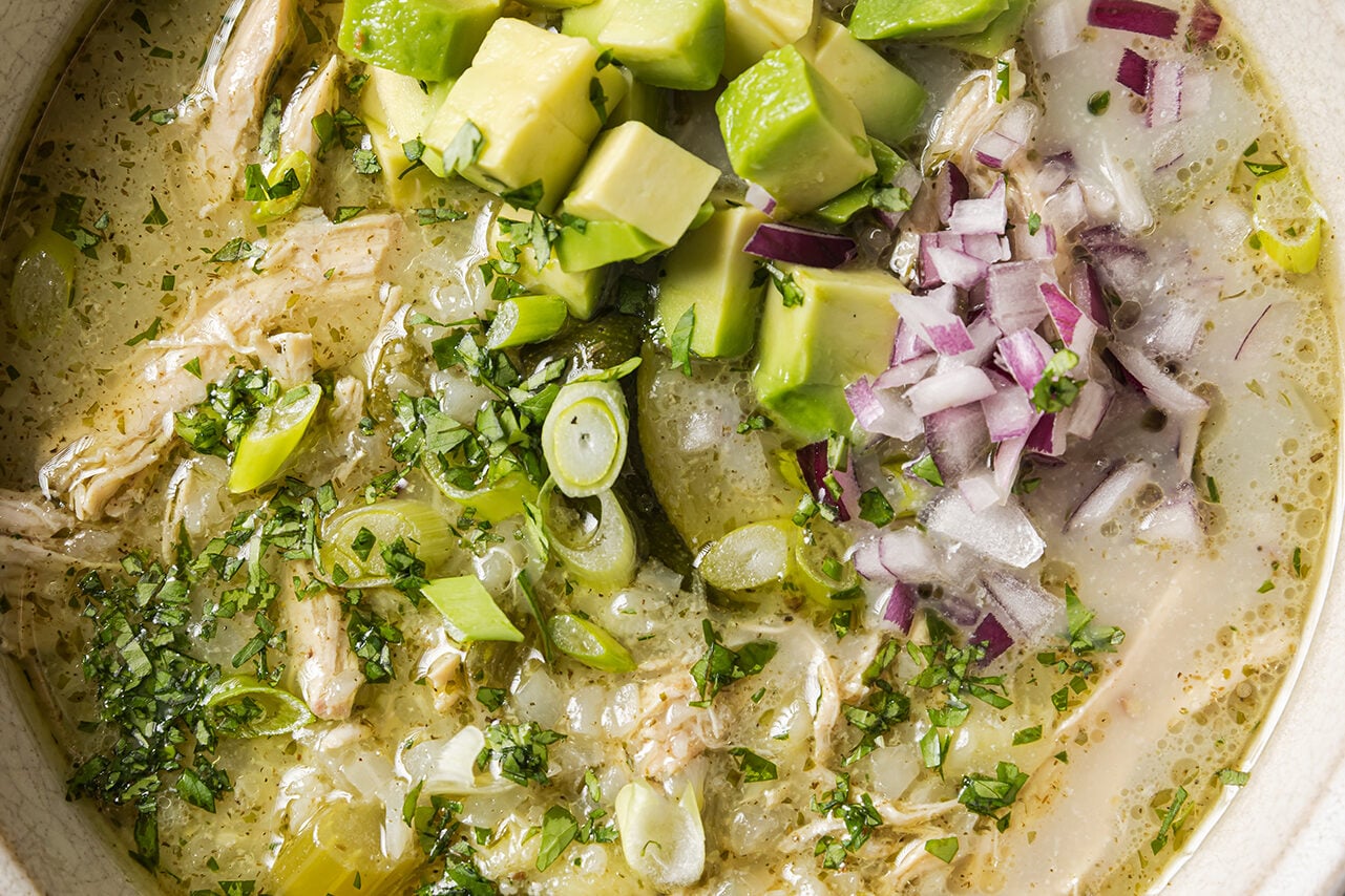 A close up of white chicken chili on a counter topped with onion and avocado.