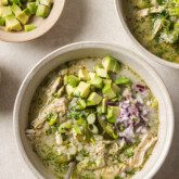 Three bowls of White chicken chili on a counter topped with onion and avocado.