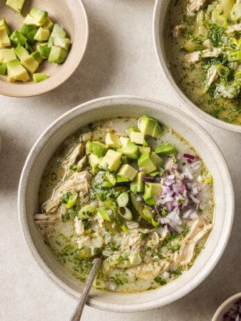 Three bowls of White chicken chili on a counter topped with onion and avocado.