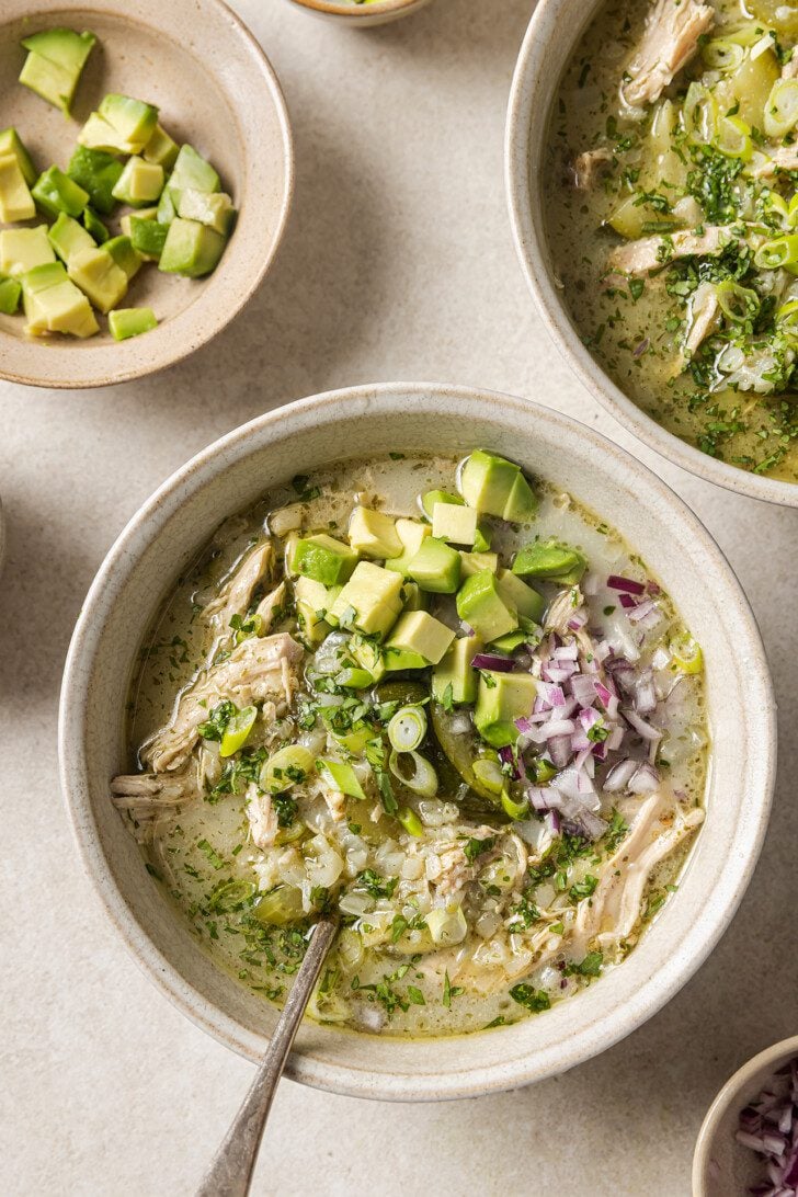Three bowls of white chicken chili topped with red onion and avocado and ready to be eaten.