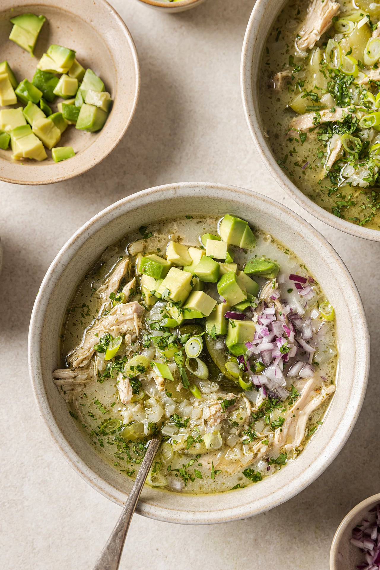 Three bowls of White chicken chili on a counter topped with onion and avocado.