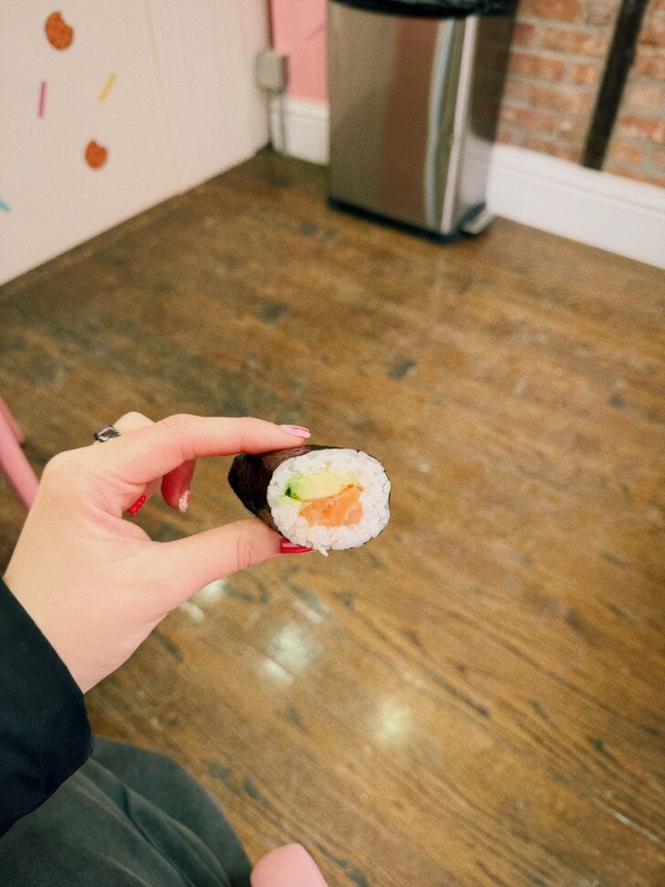 A hand holding a salmon and avocado hand roll