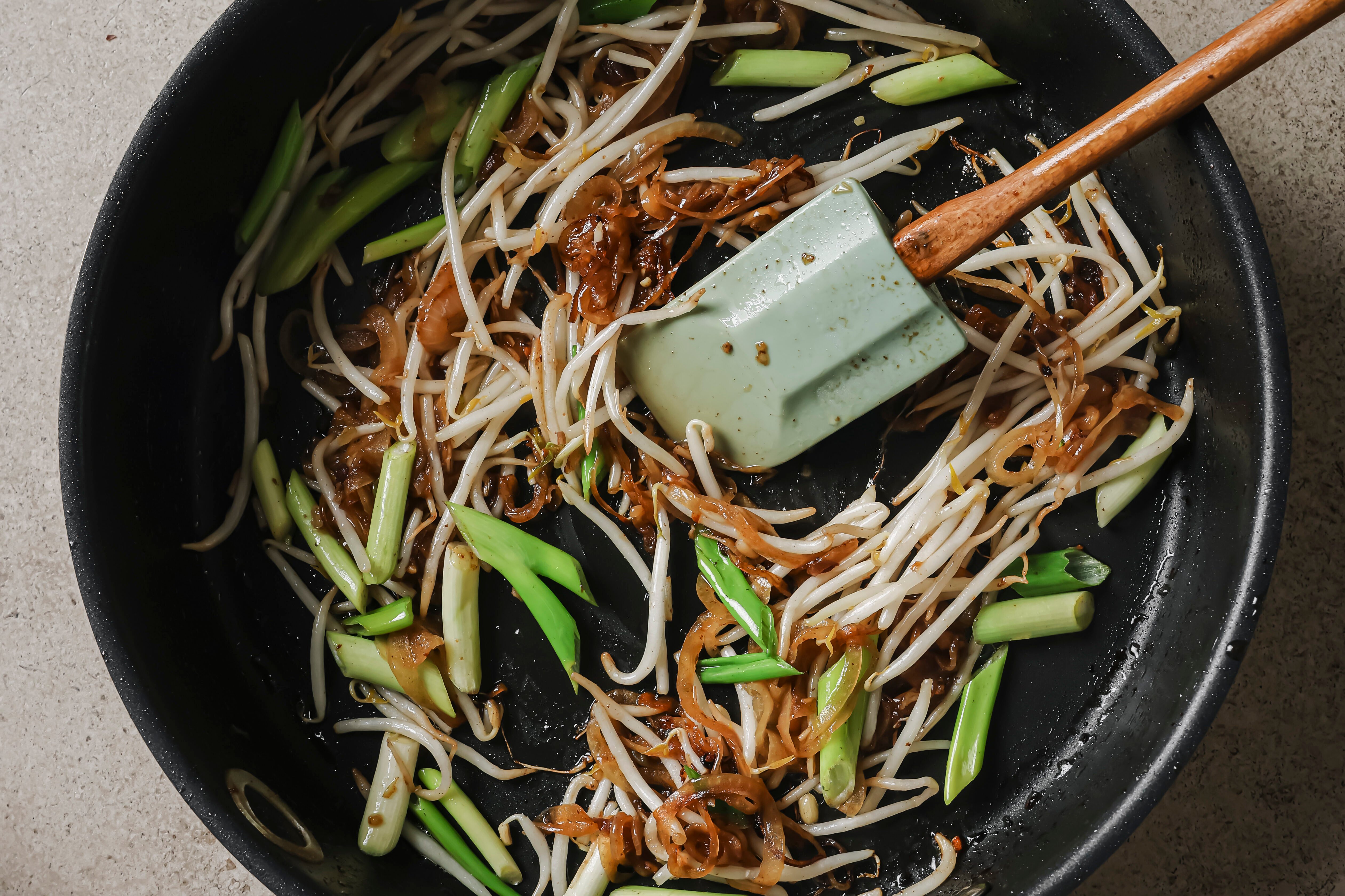 Bean sprouts, green onion and garlic cooking in a large pan.
