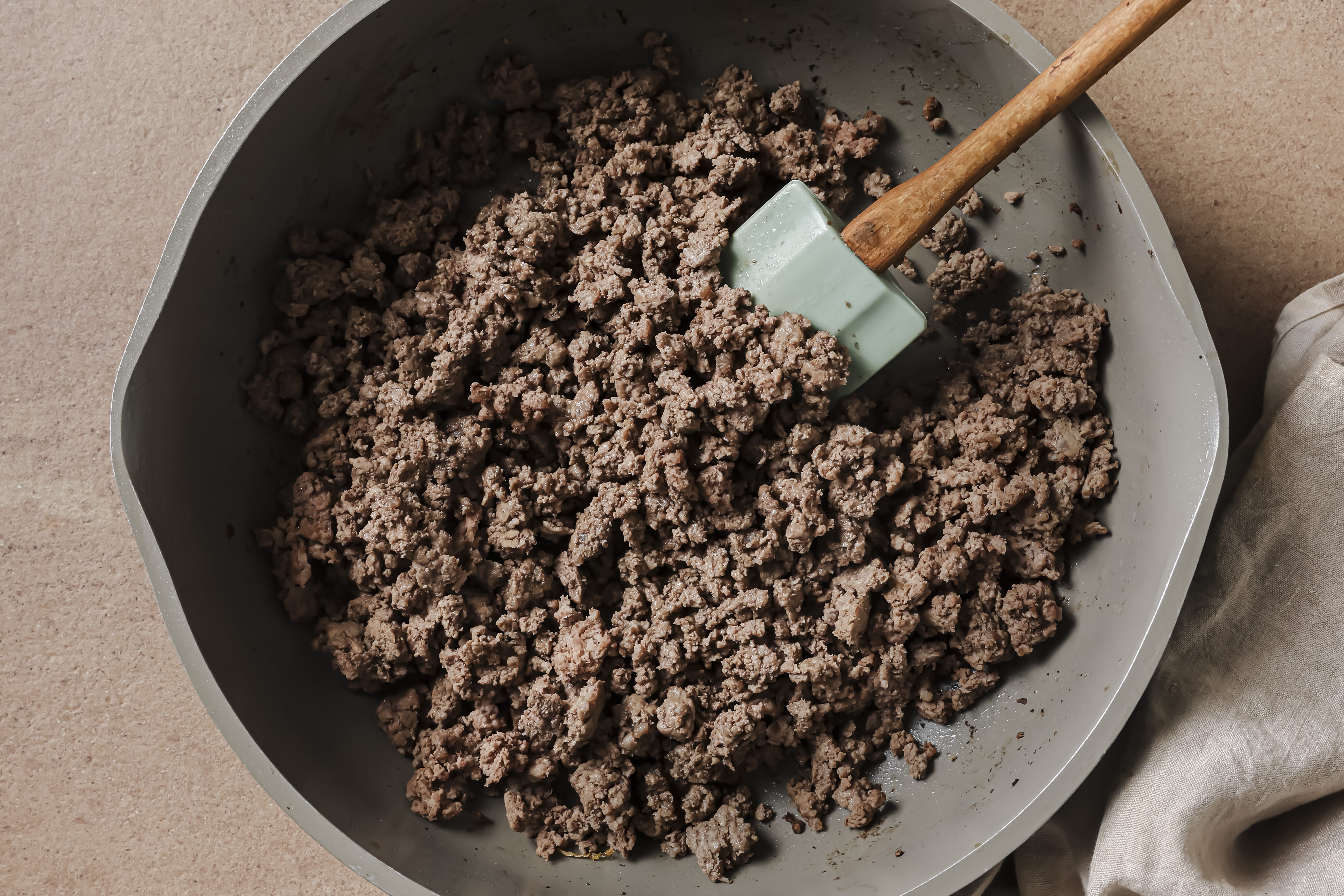 A pan with cooked ground beef with a spatula in it.