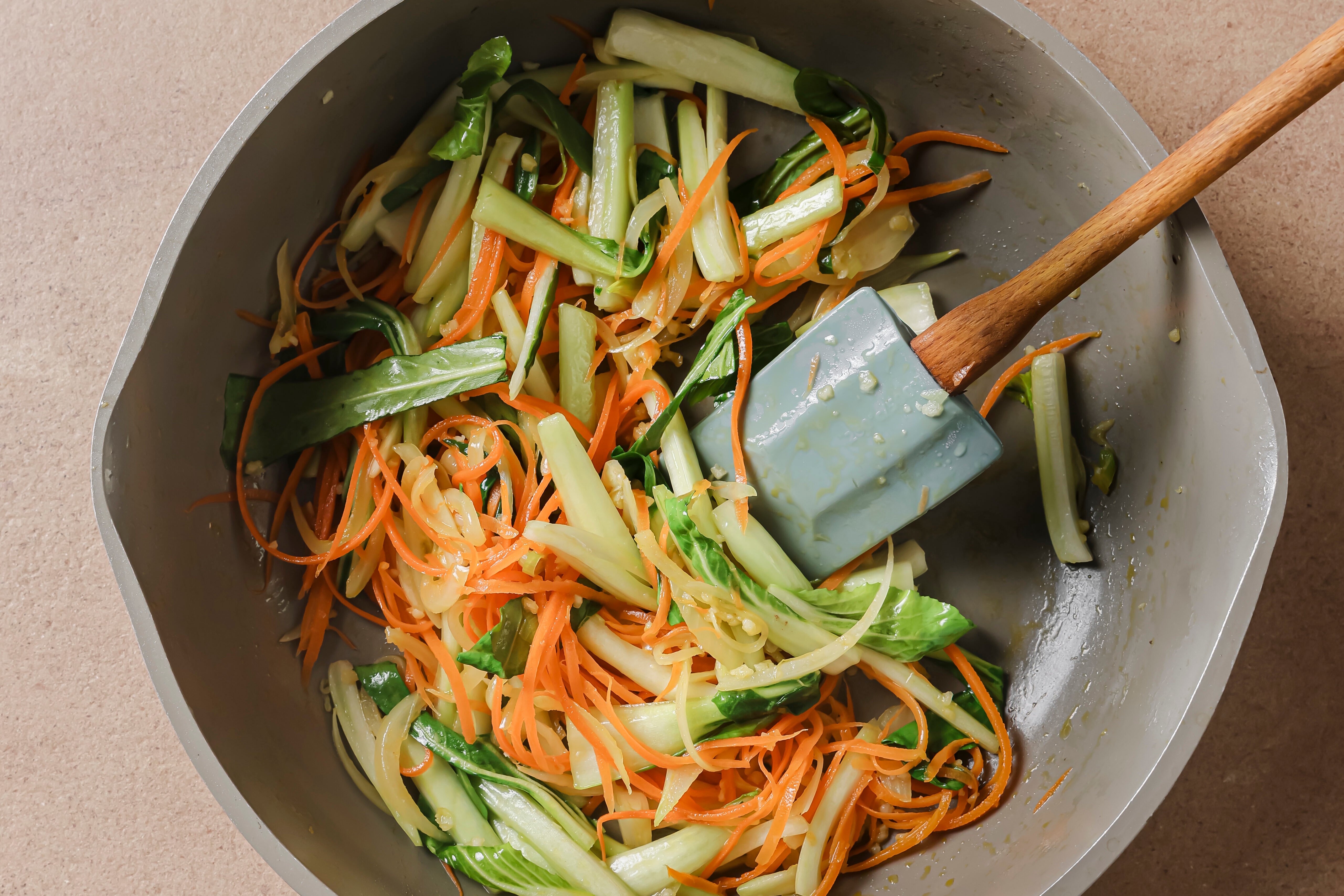 A pan with sauted veggeis with a spatula in it.