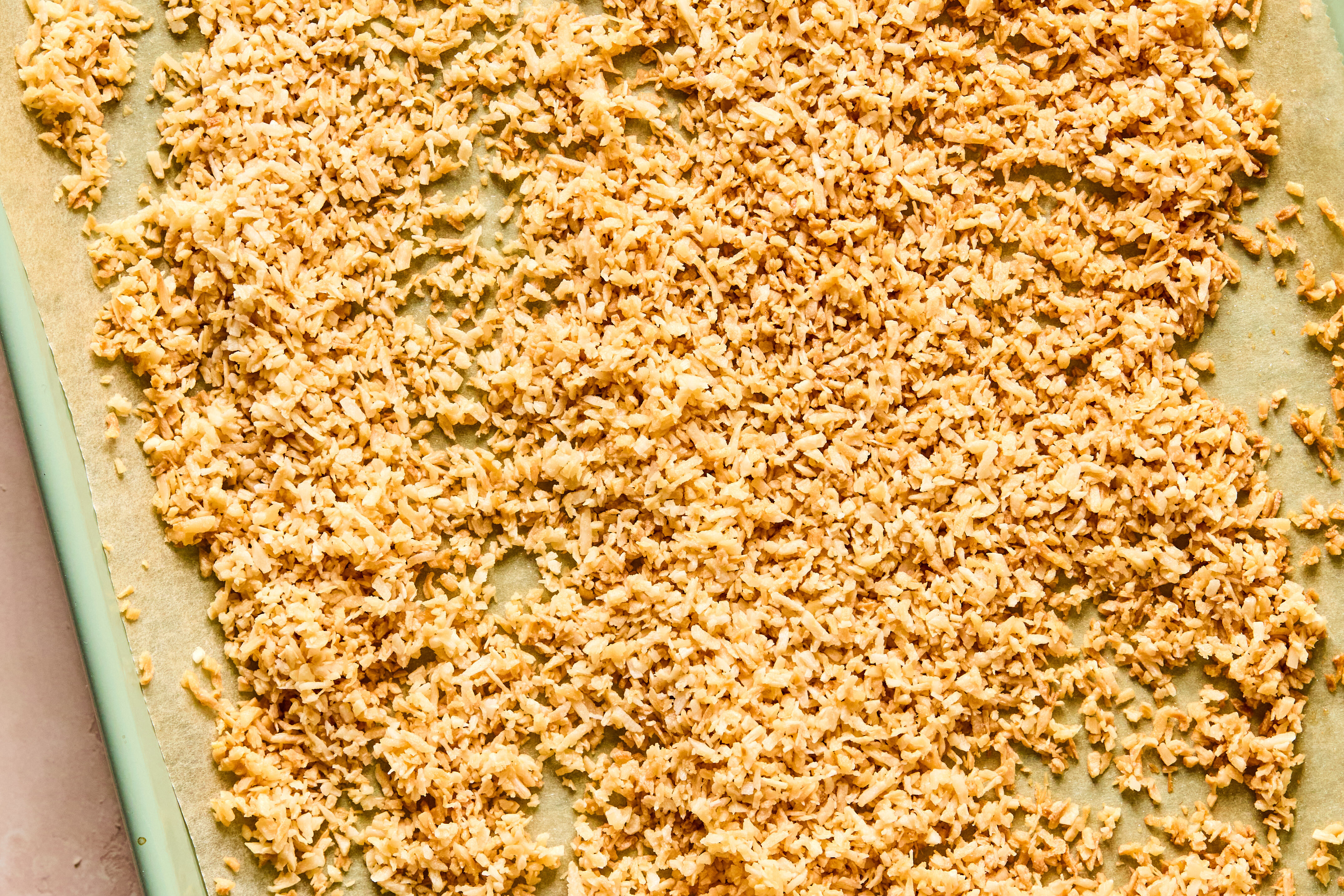 A sheet pan with parchment paper and coconut after toasting in the oven.