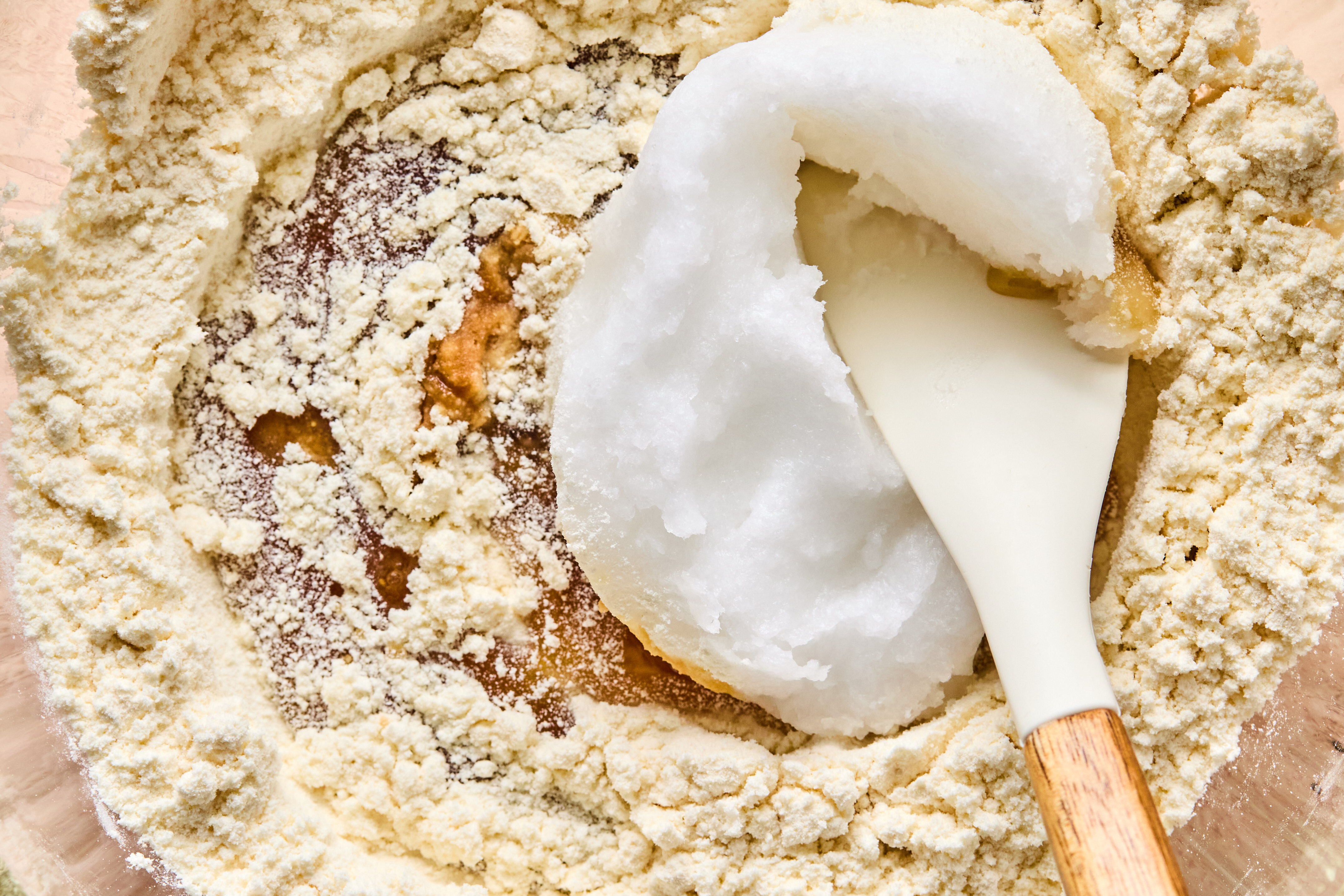 The dry and wet ingredients being mixed by a spatula in a glass bowl.