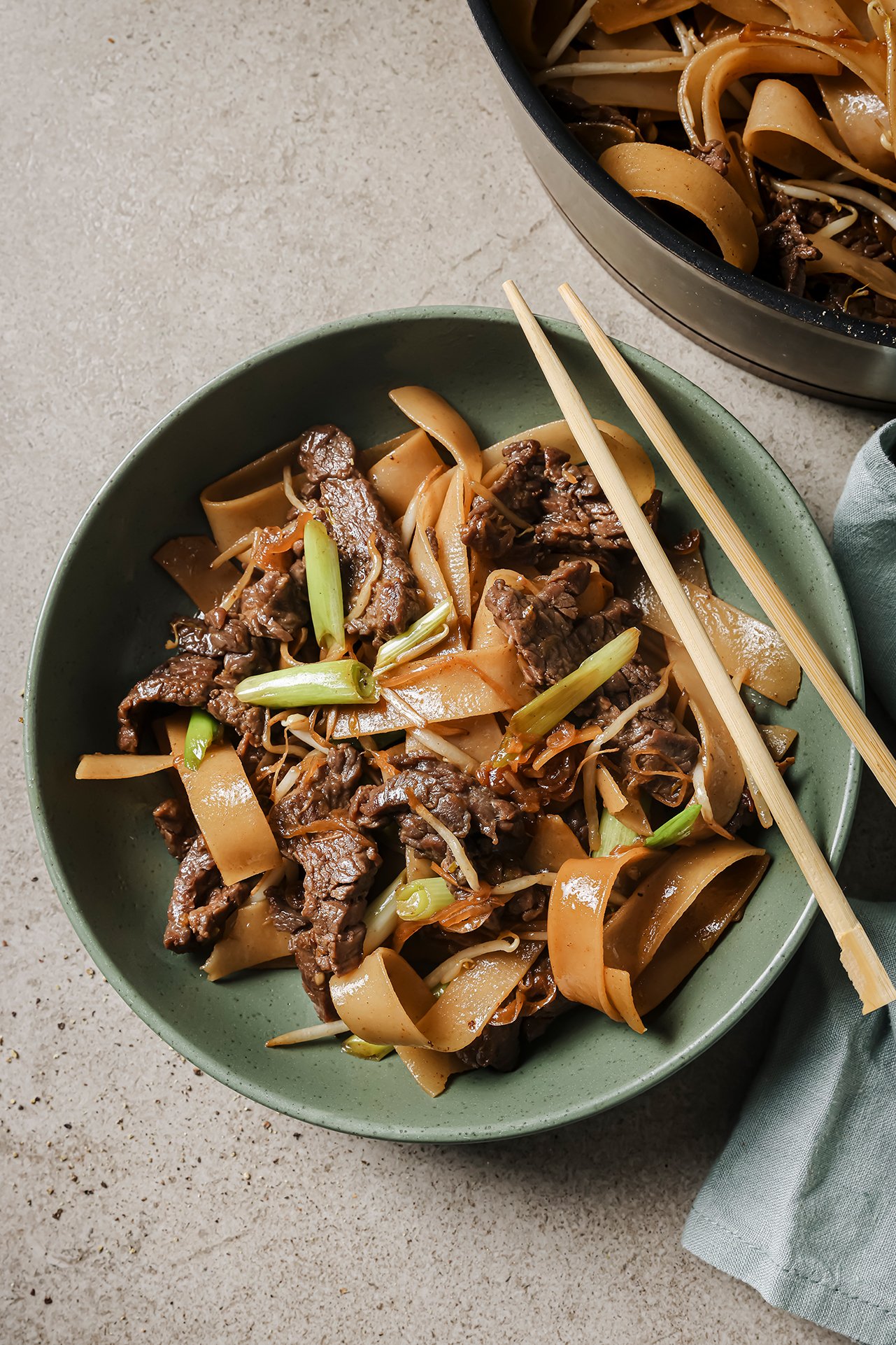 Beef chow fun in a large shallow green bowl with chopsticks.