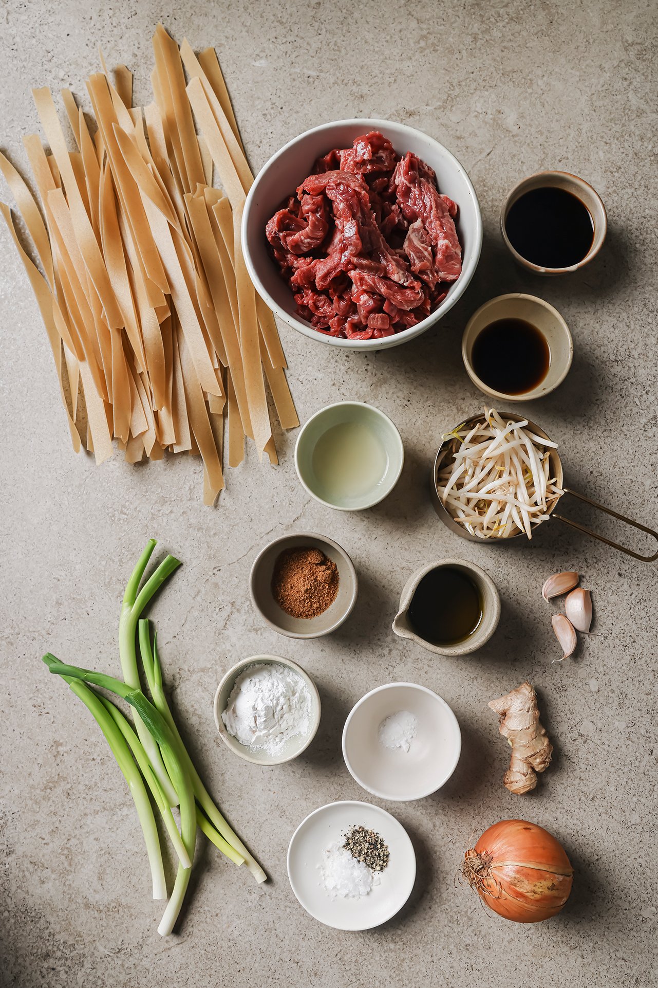 Beef chow fun ingredients laid out on a beige background.