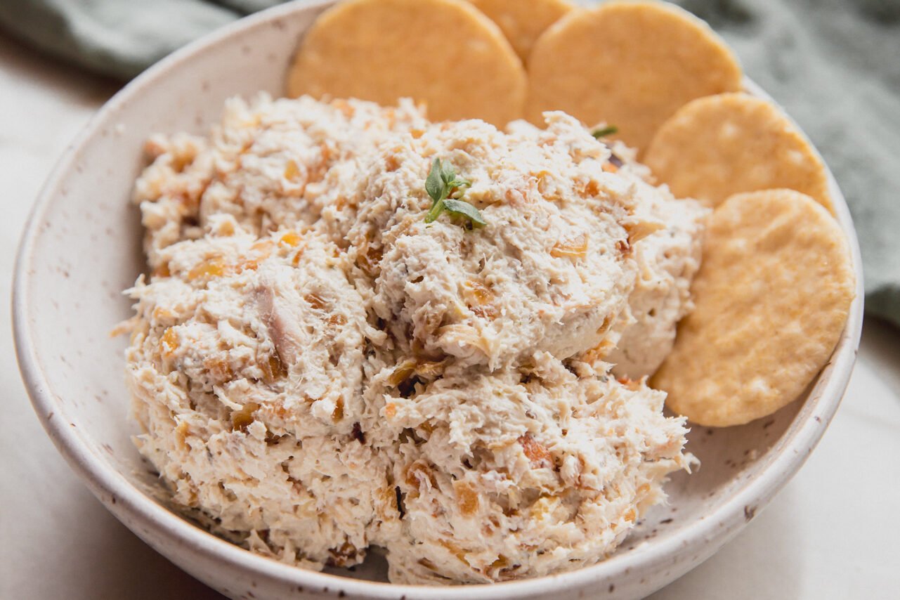 A white bowl with a serving of chicken salad and crackers in it.