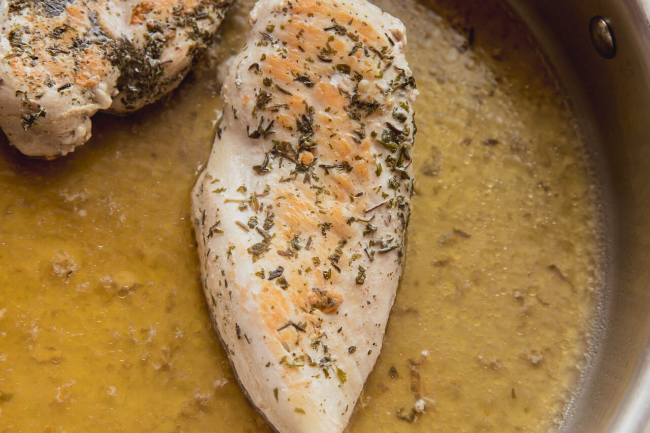 Chicken breasts in a saute pan with chicken broth and lemon juice after cooking.