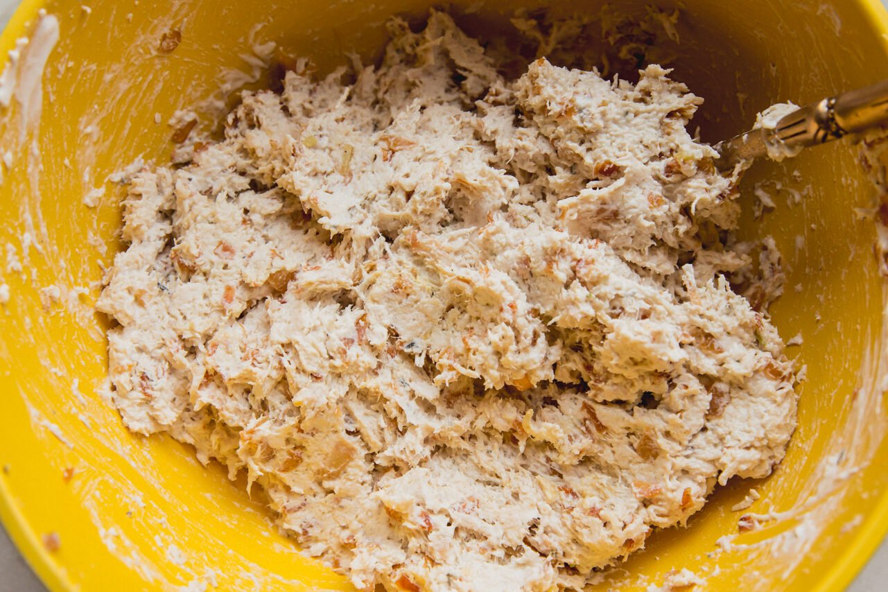 A yellow bowl with the chicken salad mixture after combining with a metal spoon.