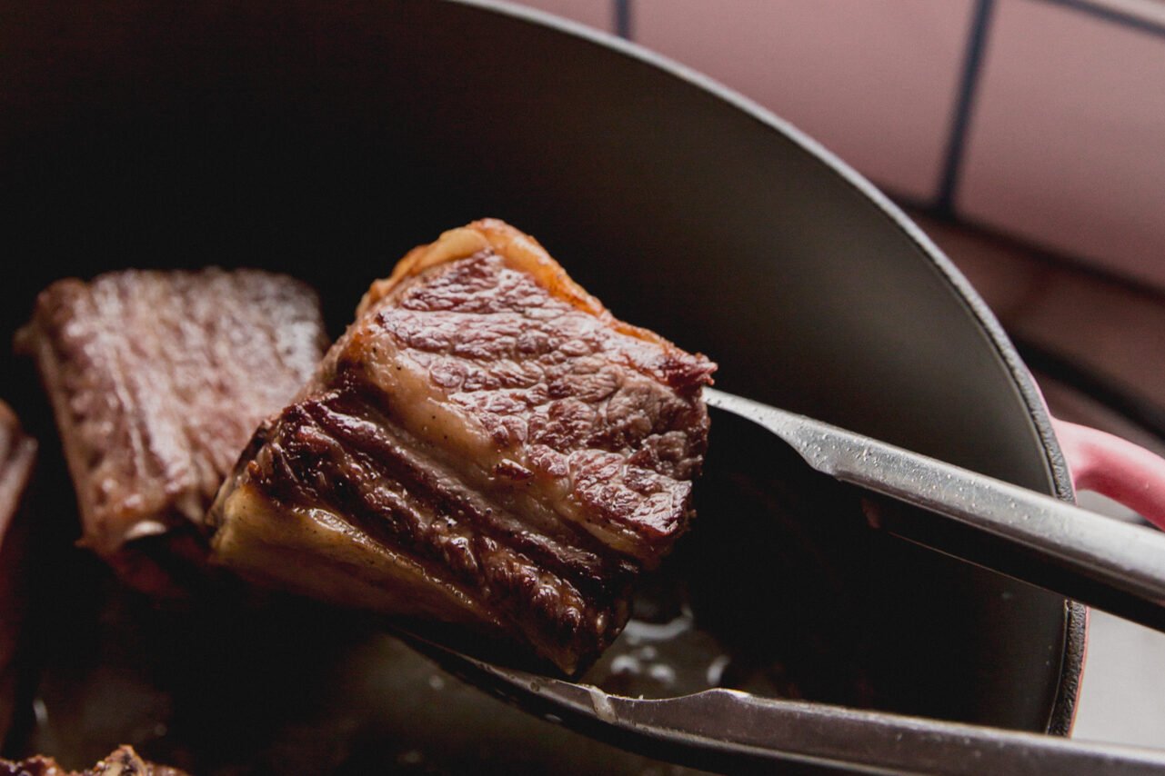 Metal thongs searing short ribs in the Dutch oven.