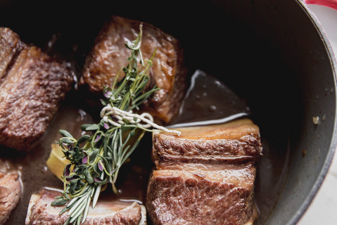 Short ribs in the Dutch oven with liquids and herbs added to it.