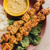 Garlic and herb chicken skewers in a bowl with dip on the side, rice and lettuce.