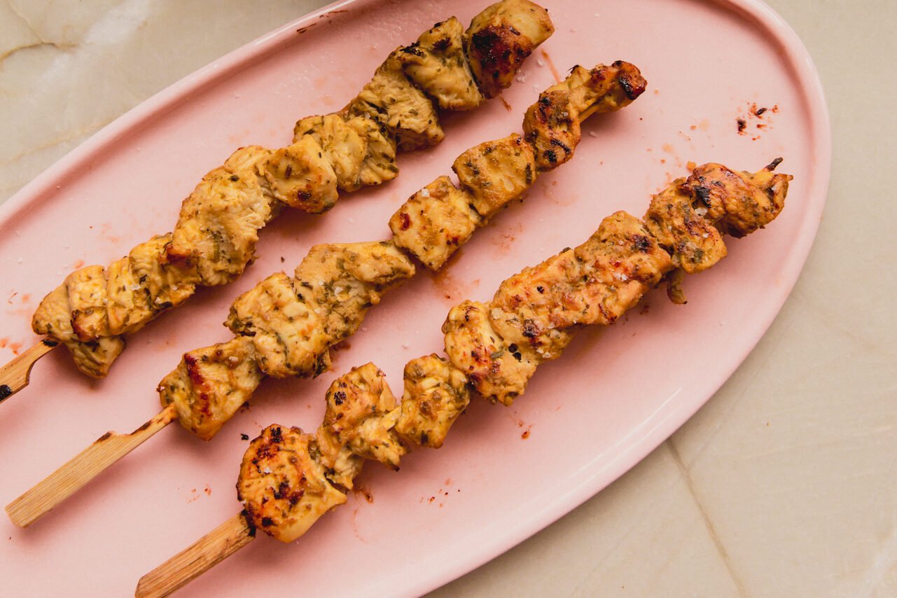Three chicken skewers on a pink platter.