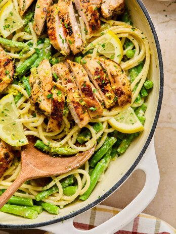 Lemon goat cheese pasta with sliced chicken thighs and green veggies in a large white pan.