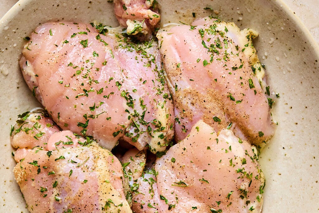 A bowl with raw chicken covered in seasoning and lemon juice marinating.