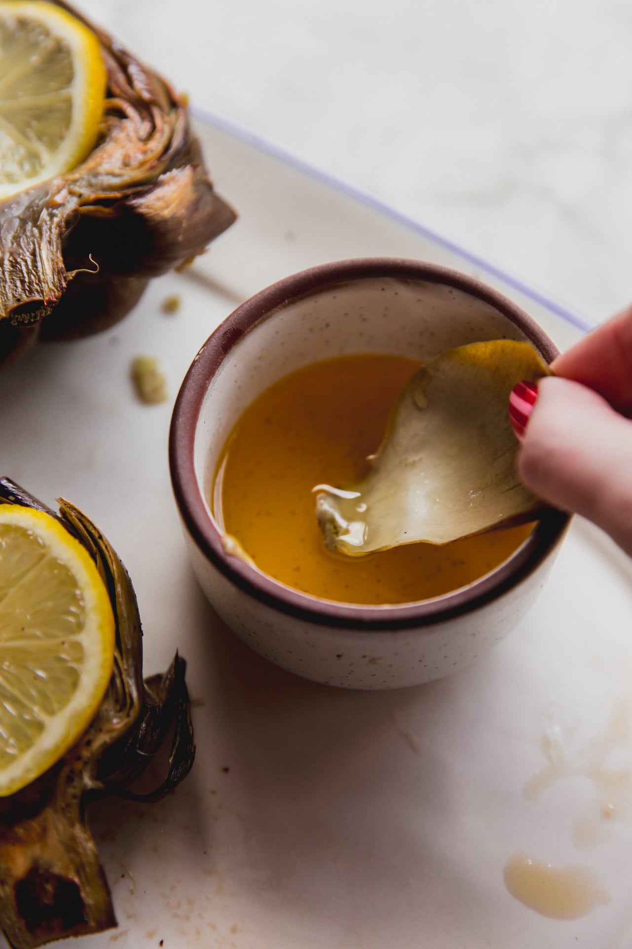 Baked artichoke leaf dipping into melted ghee.