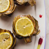 Four oven baked artichokes topped with sliced lemon and sitting on a platter.