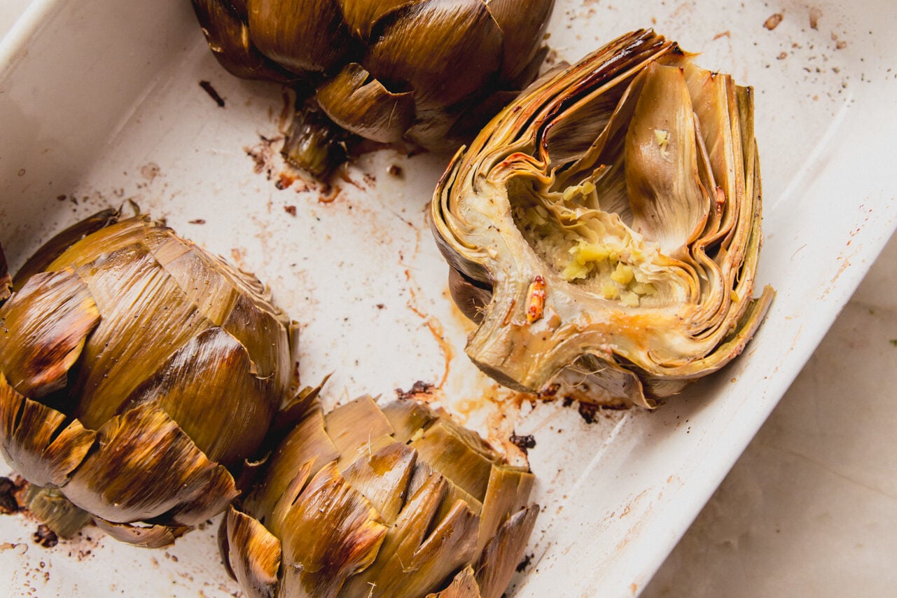 Baked artichokes halves and in a baking dish.