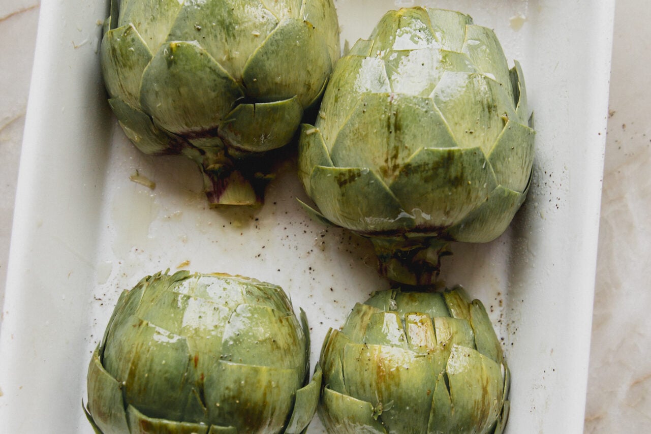 Four halved unbaked artichokes in a baking dish leave side up