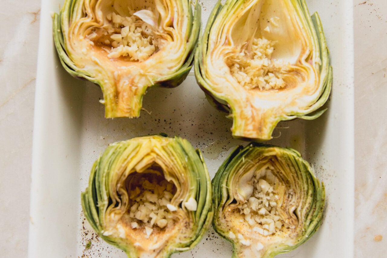 Unbaked artichokes halved and stuffed with garlic cloves.