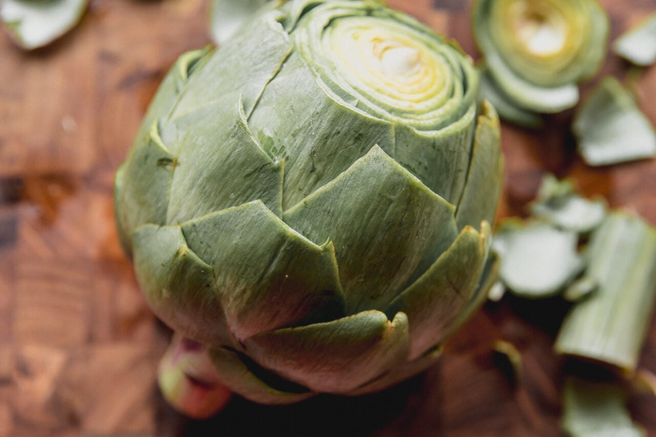 Artichoke on a cutting board with the top and leaves trimmed.