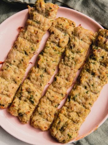 Four sheet pan chicken kebabs on a pink plate.