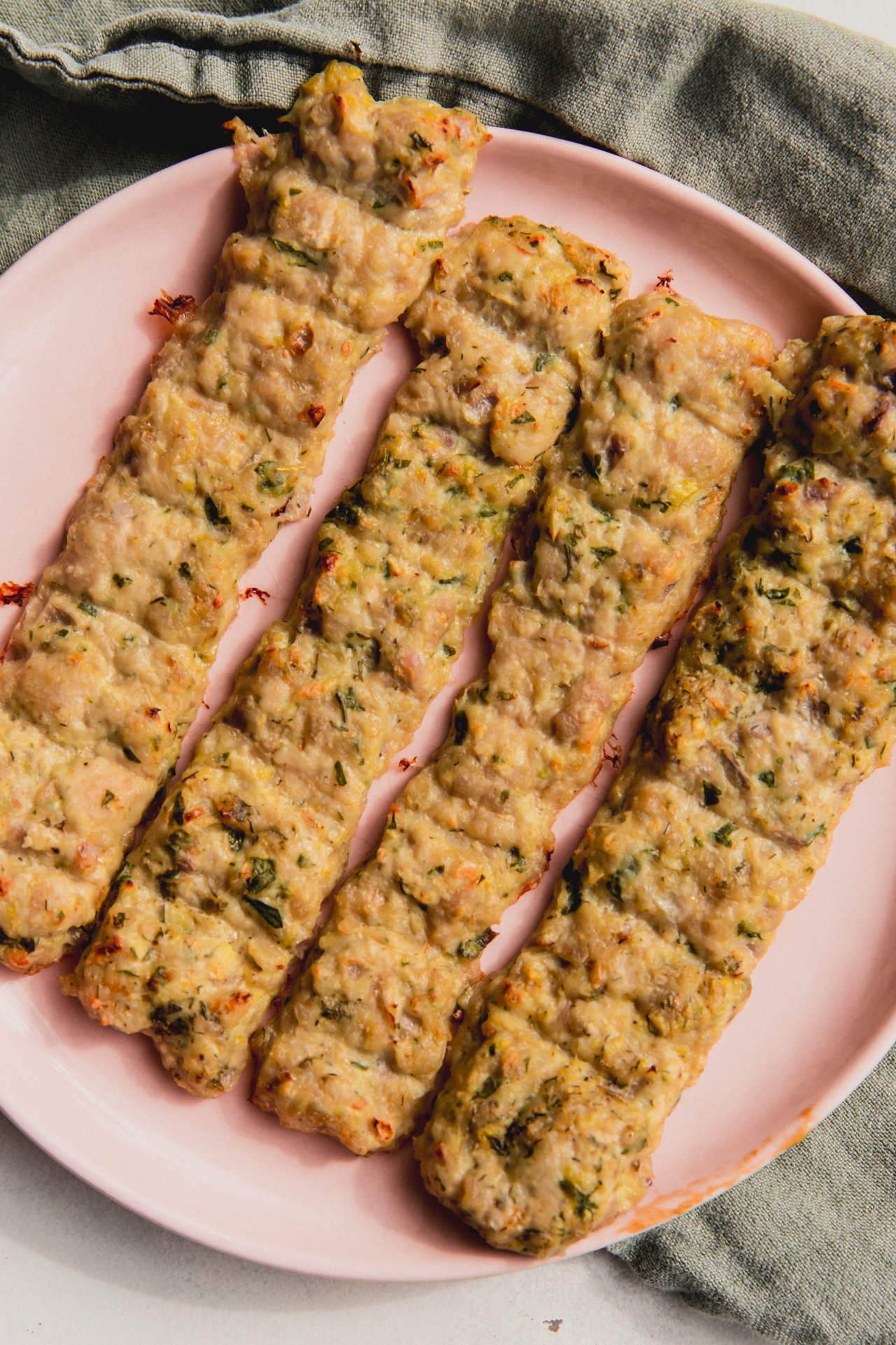 Four sheet pan chicken kebabs on a pink plate.