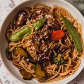 Steak noodle stir fry in a bowl with veggies and on a colorful surface.