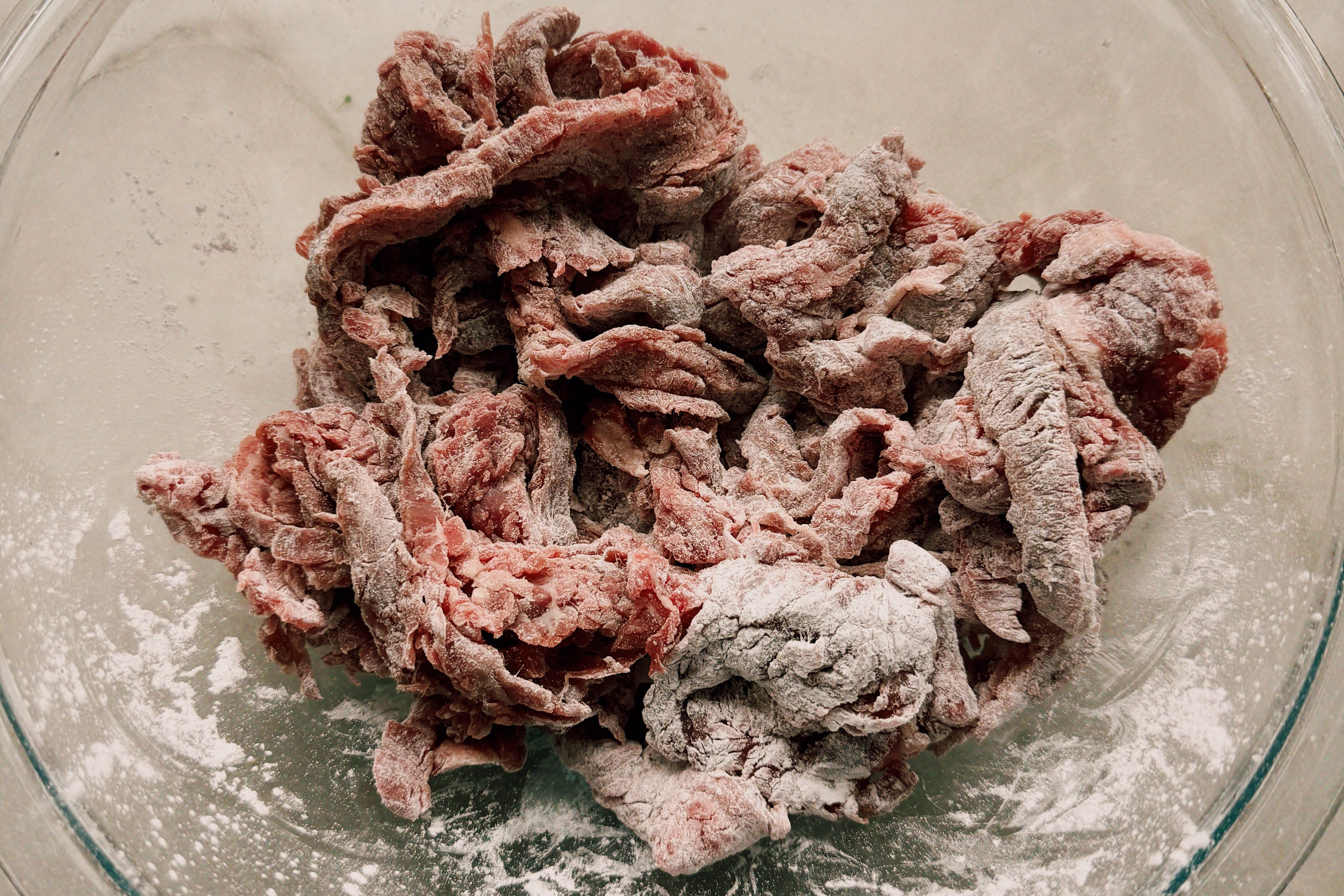 A glass bowl with beef covered in arrowroot starch before cooking.