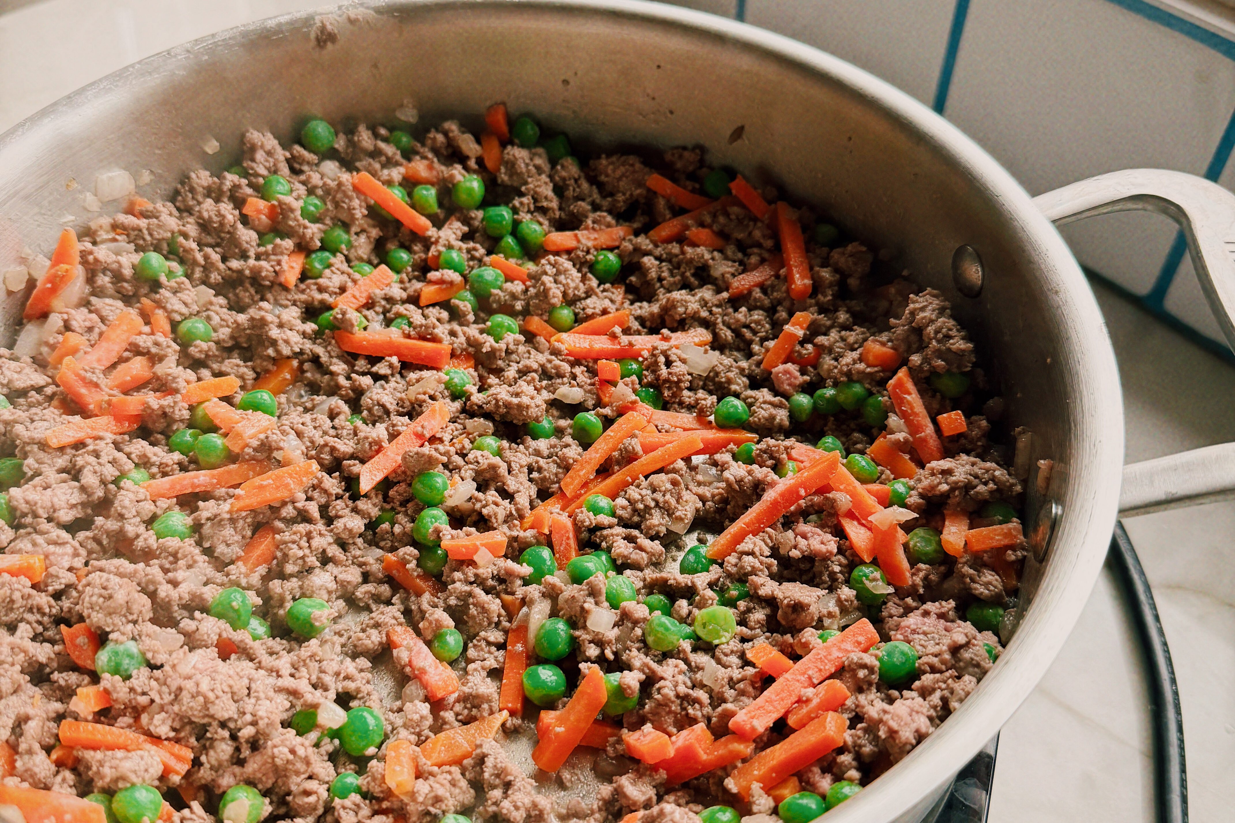 A saute pan with ground beef and veggies in it.
