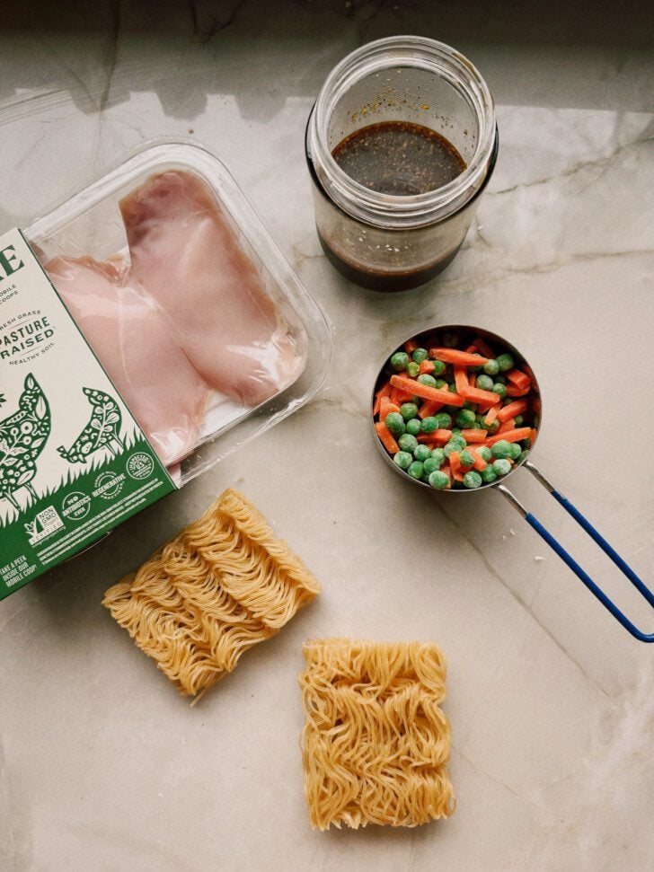 Chicken, ramen bricks, and mixed veggies on a marble counter top.
