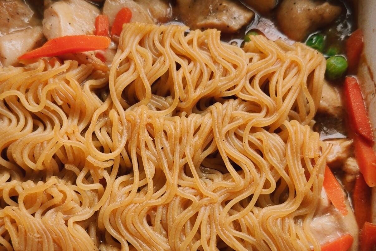Partially cooked ramen bricks in a cassrole dish with veggies and chicken.