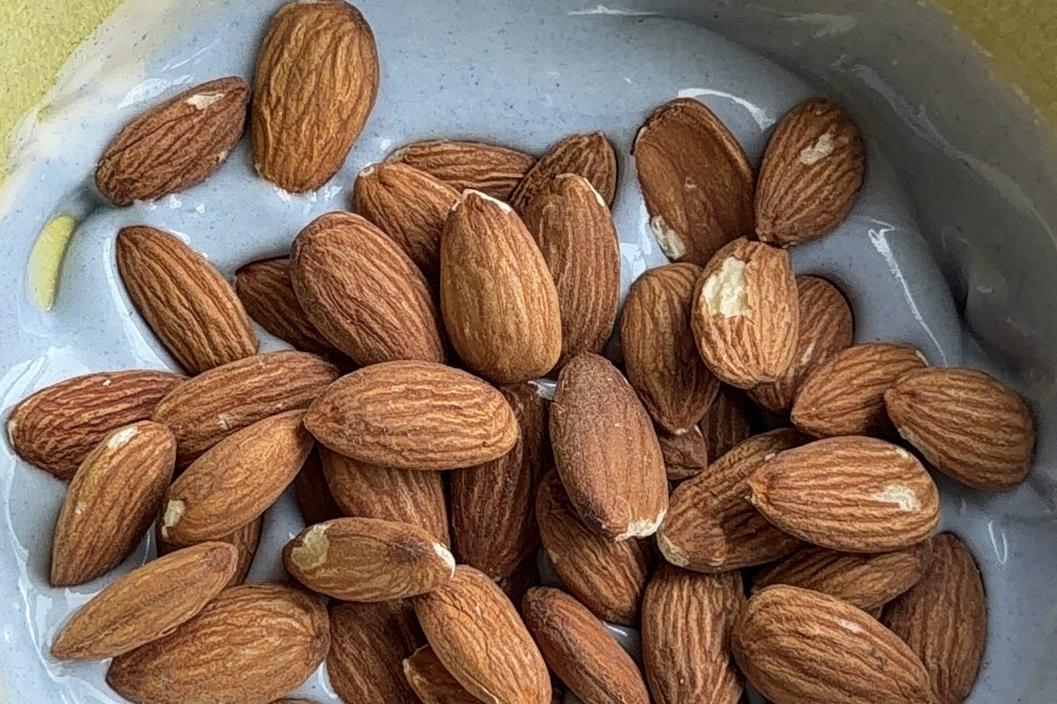 Almond added to a yellow bowl of white chocolate and blue spirulina mixture.