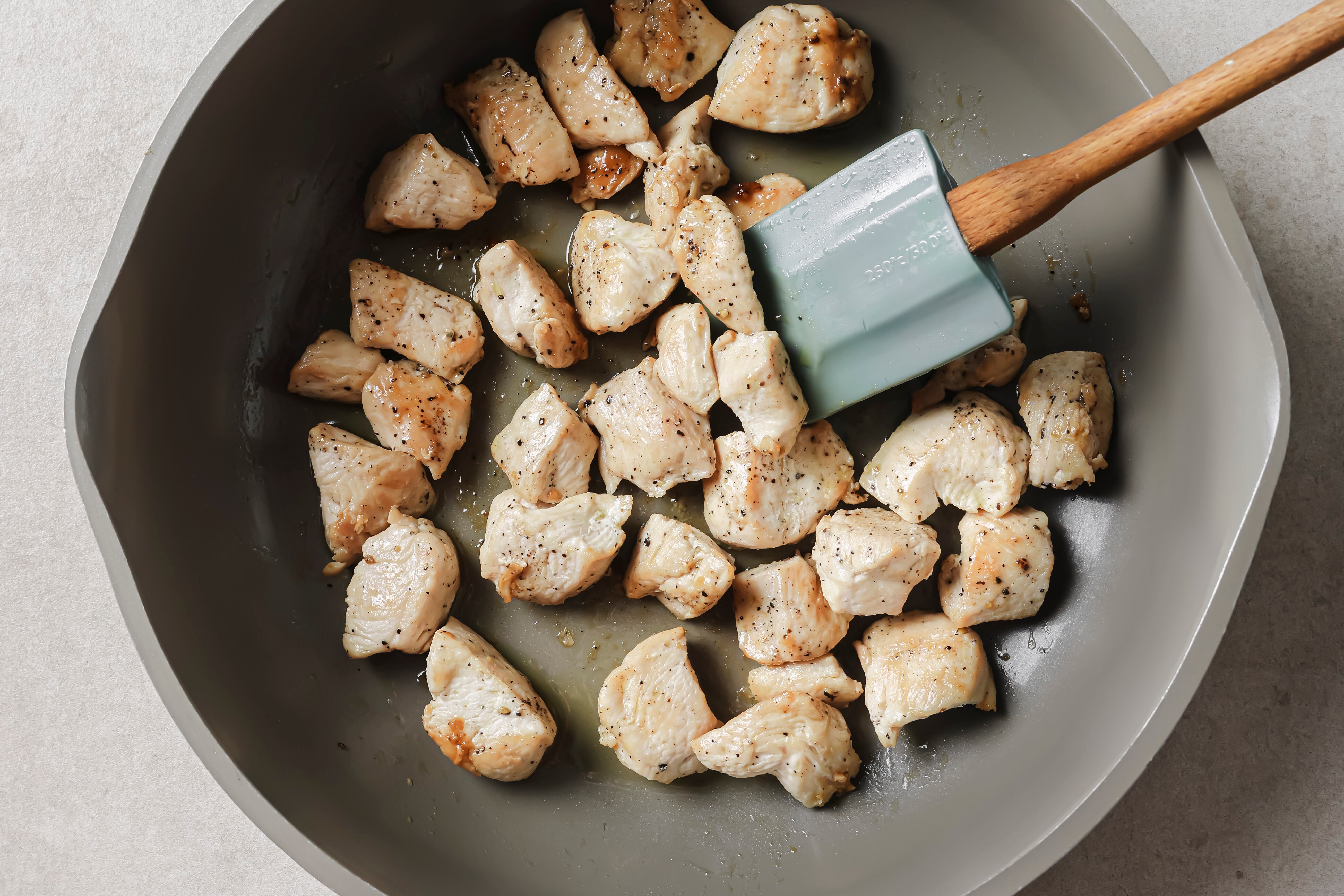 A saute pan with chicken breast cooking in it.