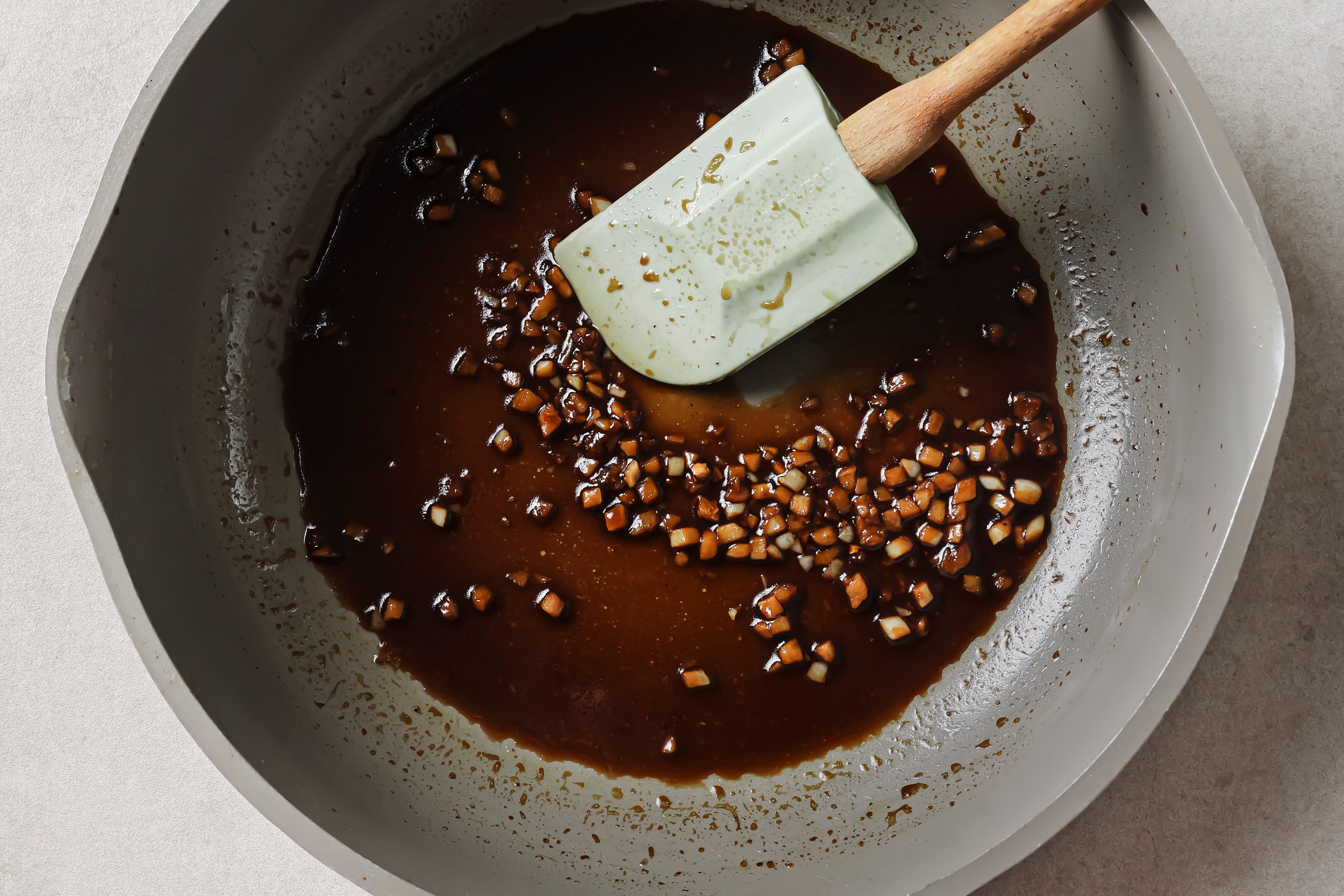 A spatula in a saute pan making the sauce for lemon & asparagus chicken skillet.